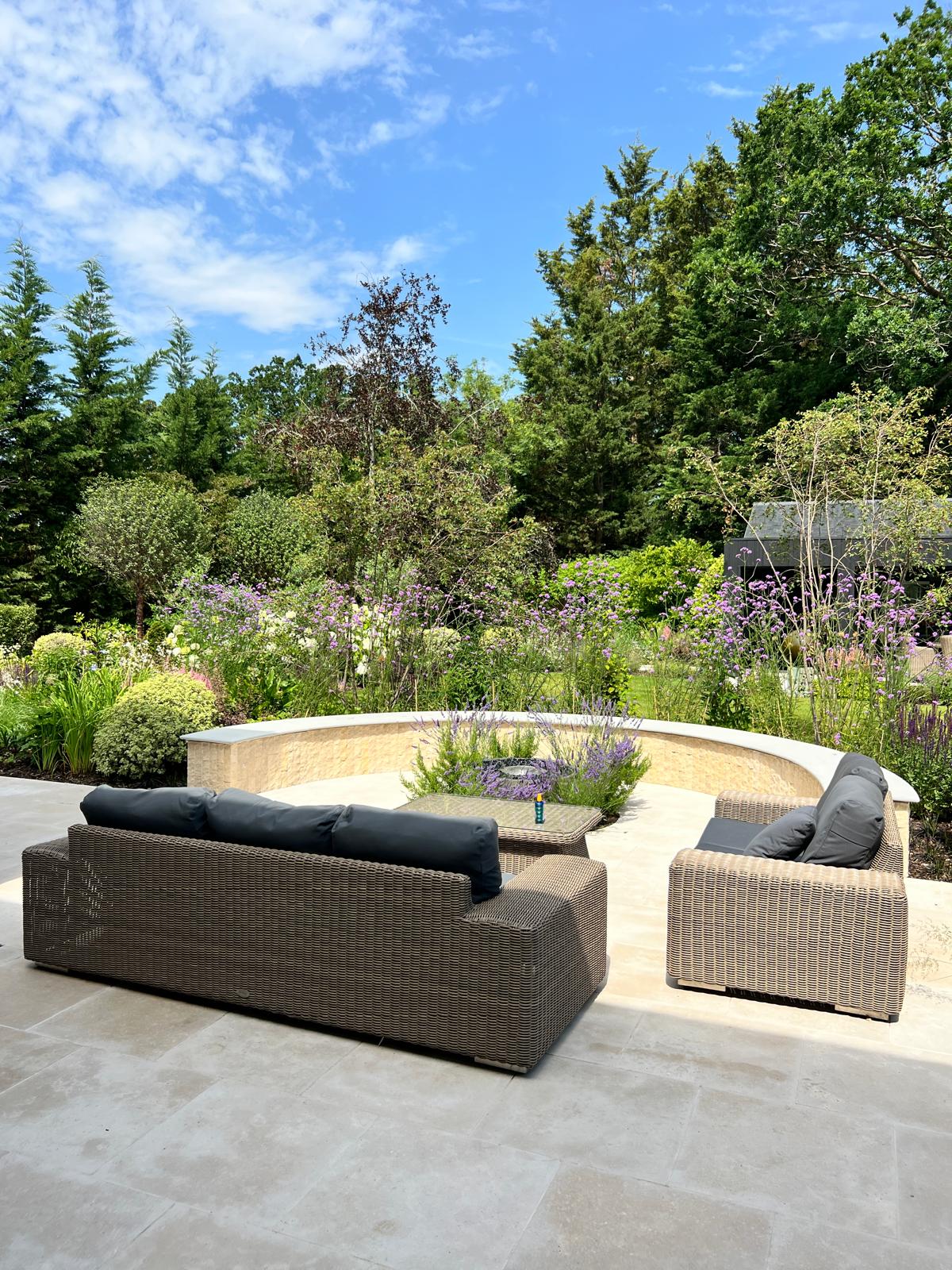 Curved stone seating wall with outdoor sofas and layered planting